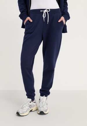 Marineblå joggebukser i myk stoff, med sidelommer og hvit snøring. Kombinert med sporty sølv- og svarte joggesko.