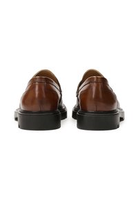 Mocasines de cuero marrón con una textura suave, suela de goma negra baja y detalles de costura sutiles, vistos desde atrás.