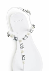 Sandalo bianco con design a T-strap decorato con gioielli chiari rettangolari e perle rotonde che adornano la cinghia. Materiale liscio con una finitura elegante.