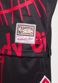 Mustapaita, jossa on punaiset painetut kirjaimet, ja siinä on kudottu etiketti, jossa lukee "Hardwood Classics" merkiltä Mitchell & Ness.