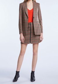 Geruite blazer in bruin, rood en groene tinten, gecombineerd met een oranje top en een aangesloten minirok met een rits aan de voorkant. Zwarte enkellaarsjes.