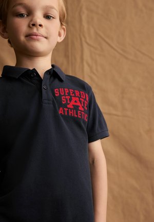 Námořnická modrá polo triko s červeným vyšitým textem "SUPERDRY STATE ATHLETIC" na levém prsu, vybavené klasickým polo límcem a krátkými rukávy.