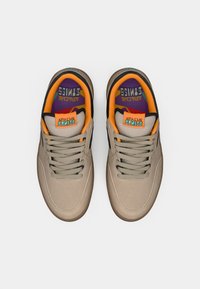 Beżowe sneakersy z teksturowaną cholewką, okrągłym noskiem i szarymi sznurówkami. Wnętrze w kolorze pomarańczowym i fioletowym z brandingiem "Apache". Podeszwa z gumy.