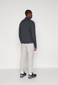 Sötétszürke, cipzáras dzseki magas gallérral, világos szürke, szűkített nadrággal és fekete sportcipővel párosítva, textúrázott anyaggal.