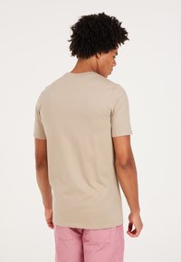 Camiseta de manga corta beige con cuello redondo. Textura suave, corte regular, combinada con pantalones cortos de pana rosa. Costuras claras.