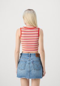 Crop top rayé en rouge, jaune et blanc ; texture côtelée avec un col rond. Porté avec une mini-jupe en denim bleu délavé.