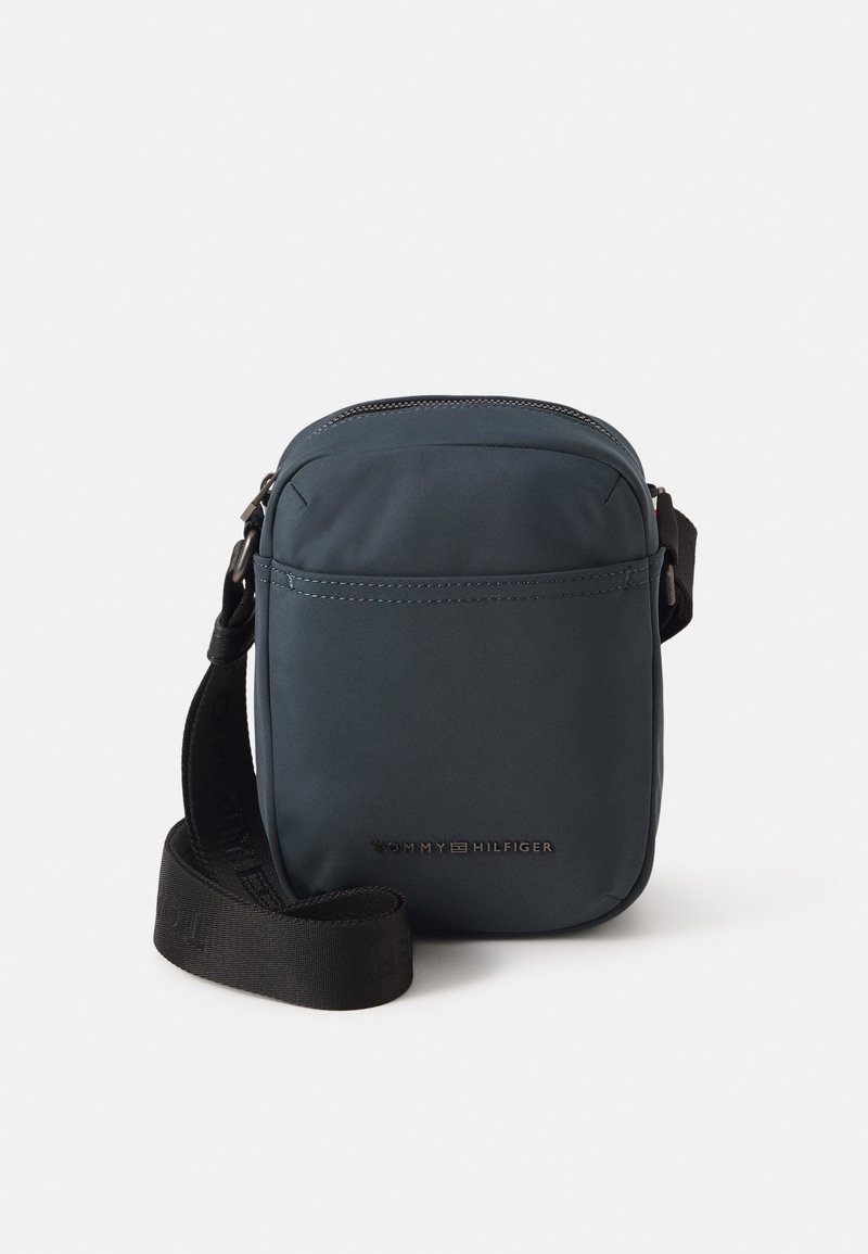 Kompaktna mornarsko plava crossbody torba od izdržljivog materijala, s zatvaranjem na rajsferšlus, podesivim remenom i suptilnim brendiranjem na prednjoj strani.