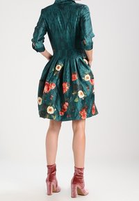 Teal dress with floral print, short sleeves, waist pleats, and a collar. Paired with pink velvet ankle boots and block heels.