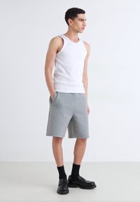 White tank top and gray shorts made of soft, textured fabric. The shorts feature side pockets and a relaxed fit, paired with black shoes.