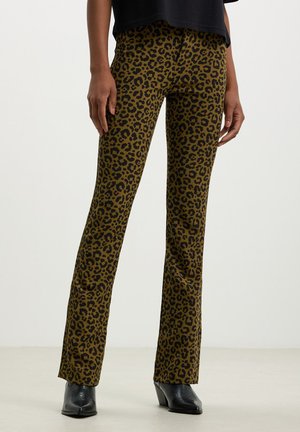 Pantaloni a zampa di elefante con stampa leopardata in verde oliva, con un motivo nero, stile aderente e una texture liscia, abbinati a stivali neri con tacco.