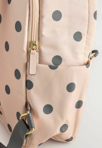 Borsa a pois in morbido tessuto rosa chiaro con pois grigi. Presenta una chiusura lampo dorata e accessori in grigio per le cinghie. Tessuto liscio e design imbottito.