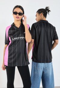 Zwart en roze atletisch poloshirt met verticale strepen en een v-hals. Model aan de linkerkant draagt een zonnebril; de achterkant heeft een effen ontwerp.