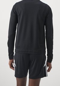 Svart atletisk jacka med långa ärmar och figurnära design, kombinerad med matchande svarta shorts med vita sidostripar. Mjuk textur.