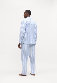 Set de pijamale în dungi, de culoare albastru deschis și alb; are mâneci lungi, croială lejeră și material moale cu un model de dungi verticale.