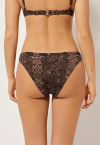 Bikini spodní část s hnědým hadím vzorem, navržená v nízkém střihu s hladkým materiálem a minimálním pokrytím, doplněná o bezseamový finiš.