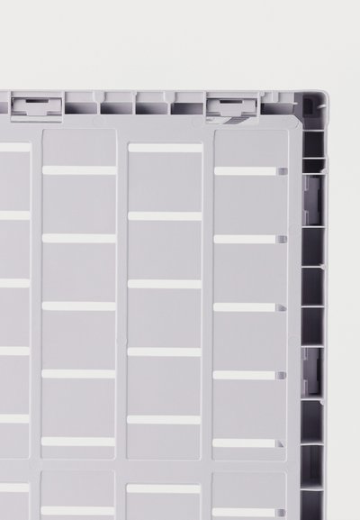 Κοντινό πλάνο ενός γκρι πλαστικού πλέγματος με ορθογώνιες υποδοχές και υφασμένη άκρη πλαισίου σε λευκό φόντο.