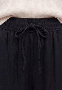 Black fabric pants with an elastic waistband tied in a bow above a light beige knitted sweater hem.