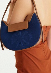 Blaue Stoffhandtasche mit einem hellbraunen Ledergriff und -klappe. Verfügt über ein gesticktes Schneeflockenmotiv auf der Vorderseite. Runde Form, lässiger Stil.