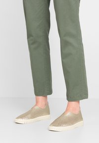 Zapatos de color verde claro tipo slip-on con un upper perforado, suela de goma blanca contrastante con dibujo visible y una textura suave.