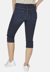 Tmavě modré džíny capri s kontrastním bílým prošitím, se zadními kapsami a těsným střihem, doplněné o bílé tenisky.