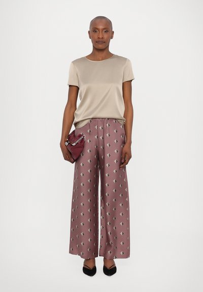 Top bege de mangas curtas combinado com calças largas estampadas em padrões geométricos em rosa e cinza, complementado por uma pequena bolsa bordô e sapatos pretos.