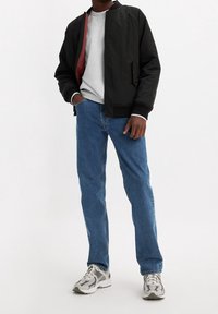 Chaqueta bomber negra con forro rojo, sudadera gris, vaqueros azules y zapatillas gris con acentos negros. Conjunta casual con un ajuste relajado.