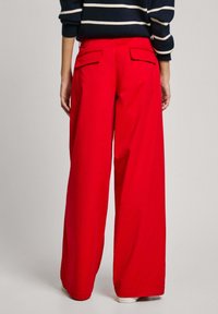 Pantaloni a gamba larga rossi in cotone. Presentano due tasche posteriori con patte. Tessuto liscio con una finitura pulita. Abbinati a un top a righe blu navy.