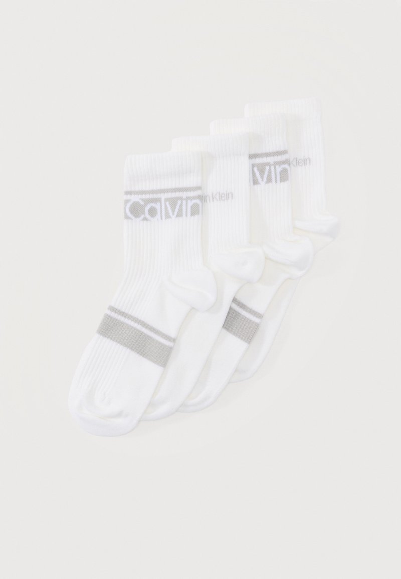 Τέσσερα ζευγάρια λευκές κάλτσες πληρώματος με ανάγλυφη υφή, γκρι τμήματα στα δάχτυλα και τη φτέρνα, και το λογότυπο "Calvin Klein" στις μανσέτες, τοποθετημένα το ένα επάνω στο άλλο.