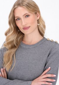 Maglione grigio a maglia con scollo rotondo, dotato di bottoni decorativi dorati sulla spalla e una morbida consistenza.