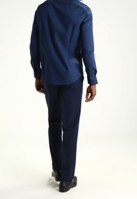 Granatowa, długą rękaw shirt o gładkiej fakturze, z mankietami zapinanymi na guziki i zaokrąglonym dołem; w połączeniu z dopasowanymi spodniami slim fit i czarnymi butami.