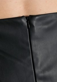 Giacchetto in finta pelle nera caratterizzato da una superficie liscia, cucitura verticale e chiusura a cerniera sul retro.