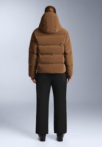 Smeđa puffer jakna s kapuljačom, kvadratnim dizajnom i labavim krojem, u kombinaciji s širokim crnim hlačama. Glatka tekstura.