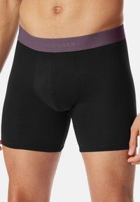 Schwarze Baumwoll-Boxershorts mit einem breiten, dunkelvioletten elastischen Bund, der mit eingeprägtem Logotext versehen ist. Eng anliegendes Design und glatte Textur.