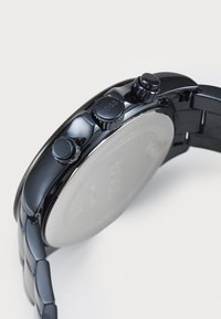 Μαύρο ρολόι χρονογράφου με γυαλιστερή μεταλλική θήκη, δύο υφασμάτινους κουμπί και μπρασελέ γυαλιστερό με ματ φινίρισμα στην πίσω πλευρά.