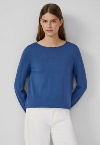 Langärmliges, blaues Strickoberteil mit rundem Ausschnitt und lässiger Passform, kombiniert mit weißen Hosen. Weiche Textur, minimalistisches Design.