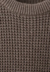 Gros plan d'un tissu tricoté marron montrant un col côtelé et un motif de points verticaux texturés.
