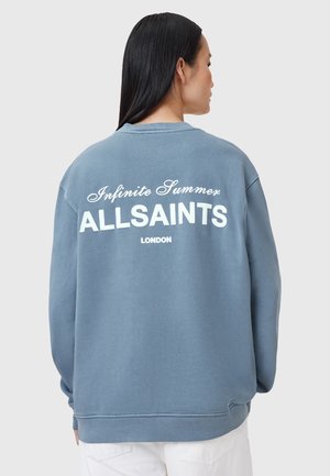 Pulover u svijetloplavom pamuku s dugim rukavima. Na leđima se nalazi bijeli natpis "Infinite Summer ALLSAINTS LONDON". Jednostavan, opušten dizajn.