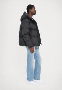 Sort pufferjakke med hætte, der har et quiltet design. Parret med lysbl�å lige ben jeans og hvide sneakers.