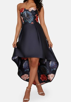 Robe sans bretelles à ourlet asymétrique en satin marine avec des motifs floraux rouges, roses et bleus. Présente un corsage ajusté et une jupe fluide pour le mouvement.