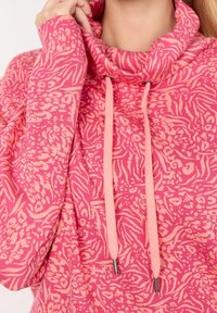 Suéter rosa con cuello de cowl, que presenta un patrón floral texturizado. Incluye cordones ajustables con puntas de metal. Tejido suave y acogedor.