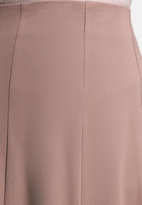 Jupe rose pâle en tissu texturé et tissé. Présente une finition lisse et des lignes épurées, mettant en valeur une silhouette cintrée.