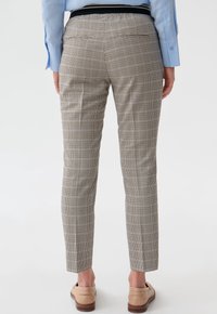 Pantalons à carreaux beiges et noirs avec une coupe slim, poches latérales et une texture lisse. Associés à des chaussures brun clair.