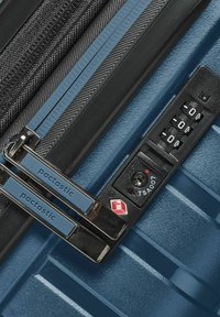 Valigia rigida blu con zip nera, doppie serrature e combinazione a manopola. Il materiale sembra resistente con una superficie texturizzata.