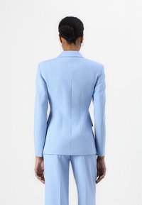 Ljust blå skräddarsydd blazer med en figursydd silhuett, skarpa slag och sömnadsdetaljer, parat med matchande byxor. Enkel, slät textur.
