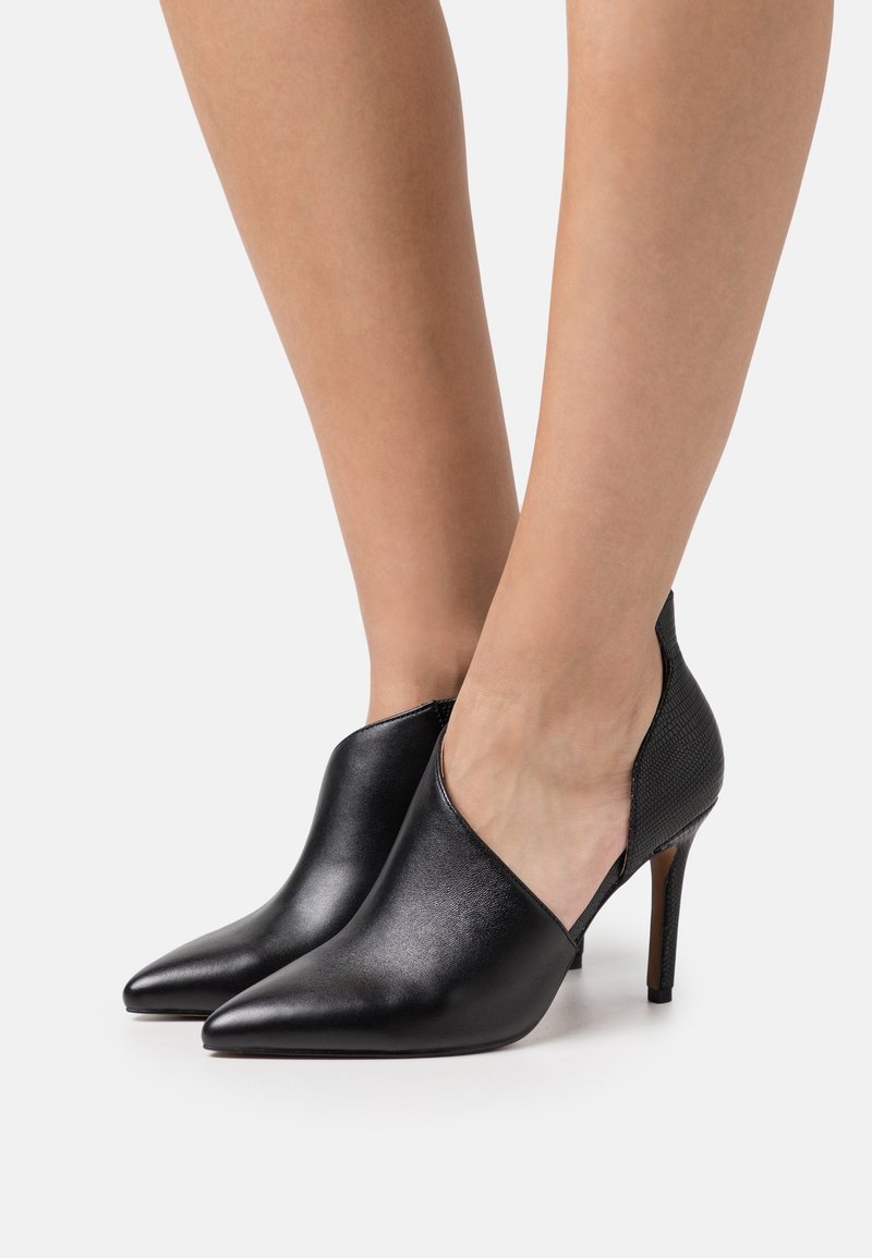 Chaussures à talons hauts en cuir noir avec bouts pointus et découpes latérales. Présentent une tige lisse et un accent texturé sur le talon.