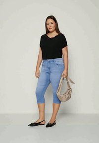 Crna majica kratkih rukava sa valovitim izrezom, svijetloplave skraćene traperice, crne balerinke i bež torba preko ramena. Jednostavan, uski, ležeran outfit.