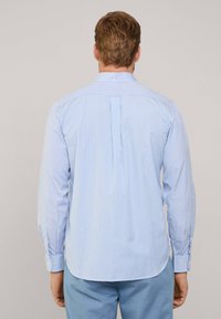 Camisa de rayas azul claro y blanca con mangas largas, puños abotonados y un yugo trasero dividido. Material suave de algodón, ajuste casual, dobladillo curvado.