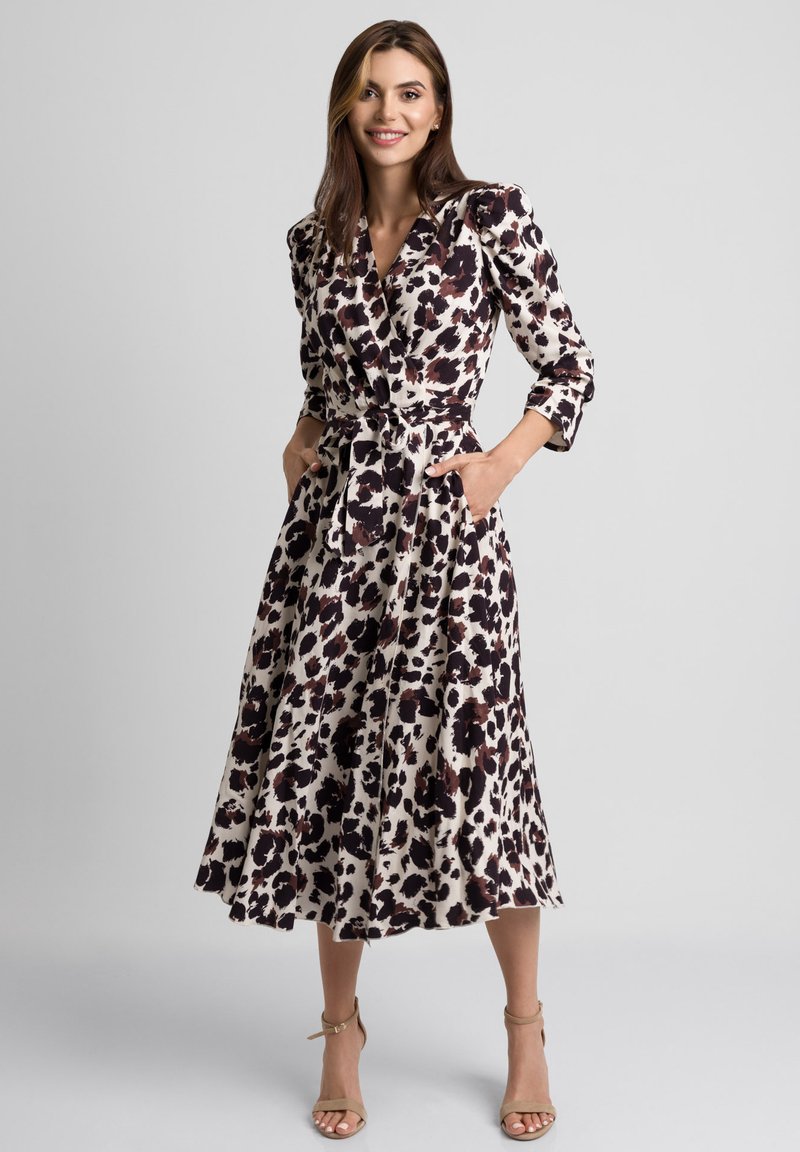 Sukienka w kolorze kremowym z ciemnobrązowym i czarnym wzorem zwierzęcym. Długie rękawy, kieszenie i wiązany pas podkreślają sylwetkę w kształcie litery A.