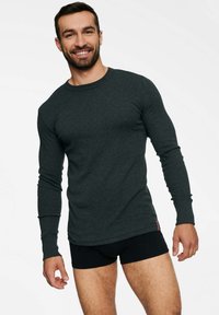 Czarnoszary t-shirt z długim rękawem, wykonany z miękkiego materia�łu, z okrągłym dekoltem i dopasowanym krojem, noszony z czarnymi figami. Prosta i gładka tekstura.