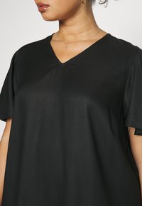 Fekete V-nyakú felső rövid ujjakkal, sima anyagból készült. Lazán illeszkedő szabás és finom textúra jellemzi. Minimalista design, minták vagy díszítések nélkül.